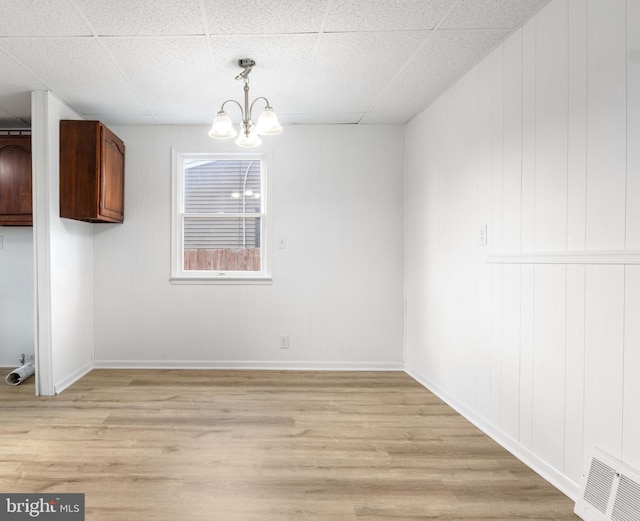 unfurnished dining area featuring a paneled ceiling, a notable chandelier, and light hardwood / wood-style floors