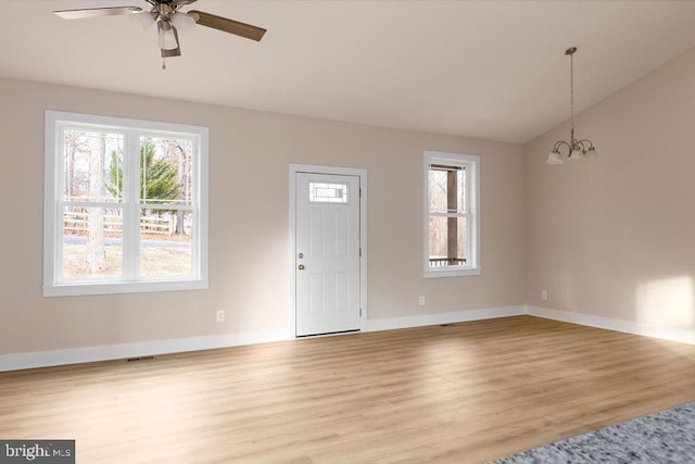 unfurnished living room with ceiling fan with notable chandelier, vaulted ceiling, and light wood-type flooring