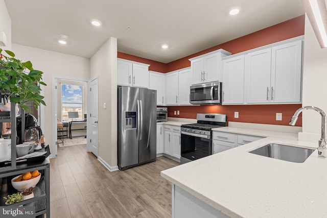 kitchen featuring light stone countertops, sink, stainless steel appliances, white cabinets, and light wood-type flooring