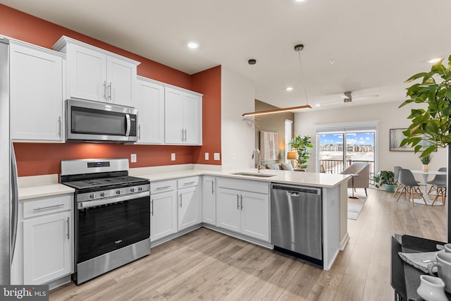 kitchen with white cabinets, sink, decorative light fixtures, kitchen peninsula, and stainless steel appliances