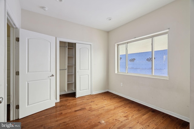 unfurnished bedroom with multiple windows, a closet, and hardwood / wood-style flooring