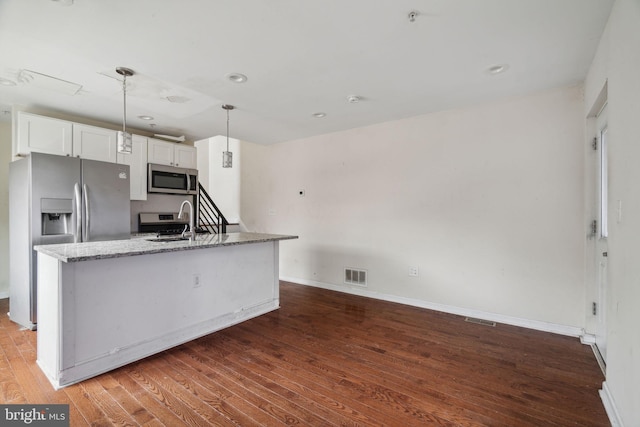 kitchen with appliances with stainless steel finishes, sink, pendant lighting, stone countertops, and white cabinetry