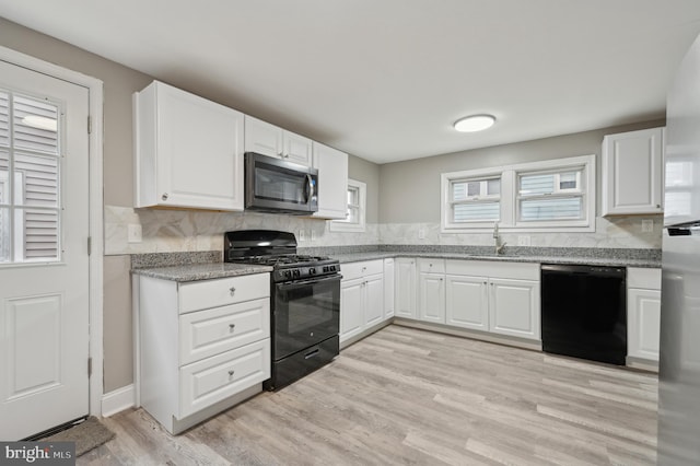 kitchen featuring white cabinetry, sink, tasteful backsplash, black appliances, and light wood-type flooring