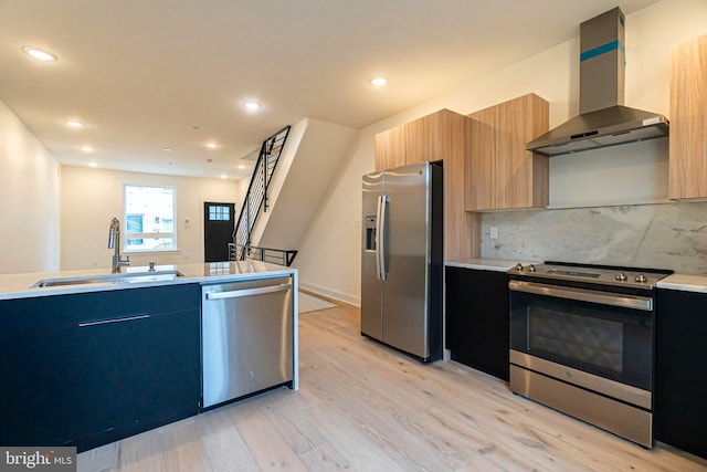 kitchen with light wood-type flooring, tasteful backsplash, wall chimney exhaust hood, stainless steel appliances, and sink