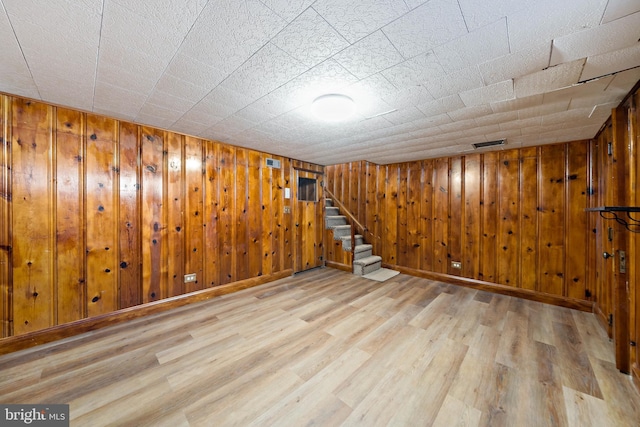 basement featuring light wood-type flooring and wood walls