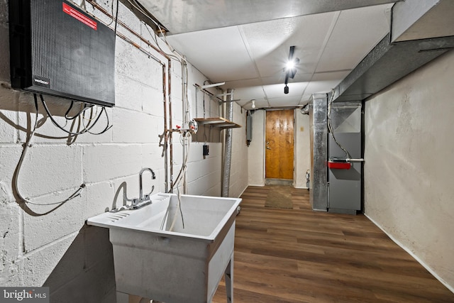 basement featuring heating unit, sink, and dark hardwood / wood-style floors