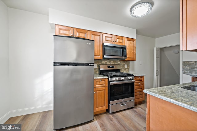 kitchen featuring decorative backsplash, appliances with stainless steel finishes, light hardwood / wood-style floors, and light stone counters