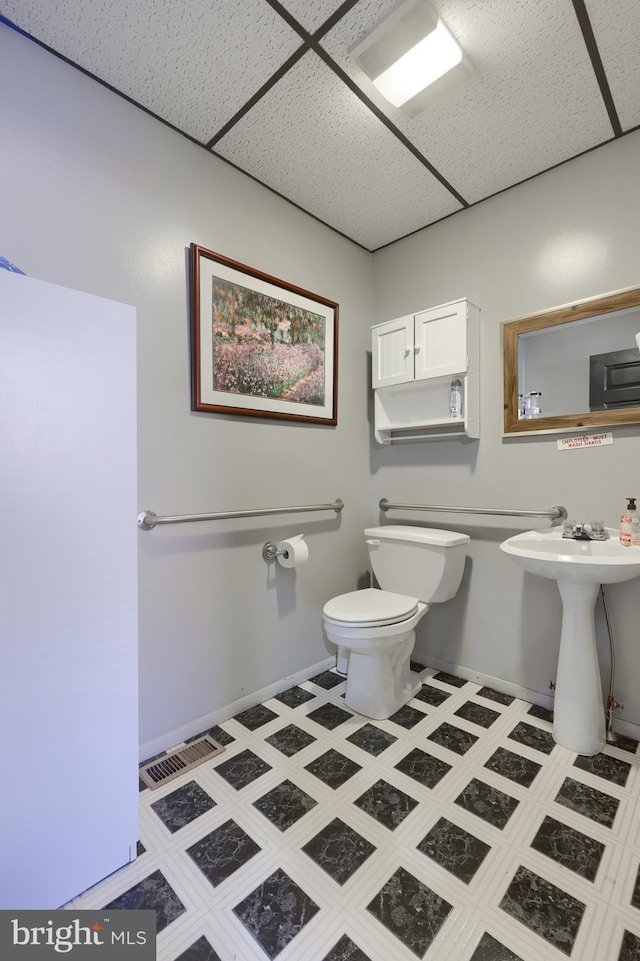 bathroom with a paneled ceiling, toilet, and sink