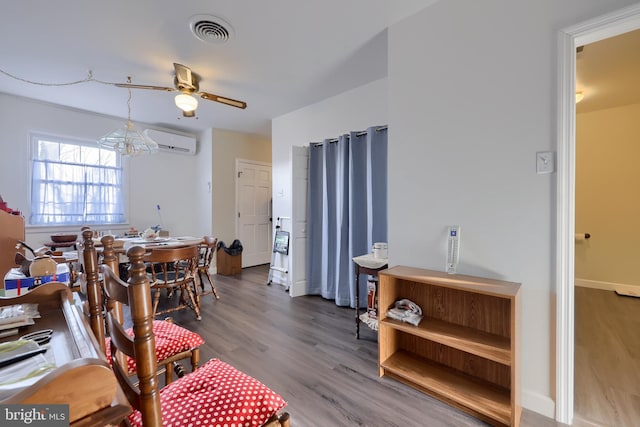 dining space featuring a wall mounted air conditioner, wood-type flooring, and ceiling fan with notable chandelier