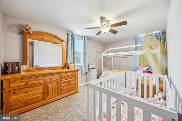 bedroom with ceiling fan, a nursery area, and carpet flooring