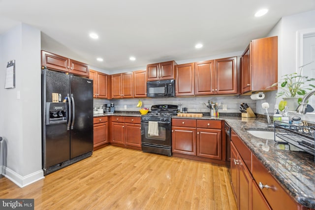 kitchen featuring black appliances, dark stone counters, decorative backsplash, sink, and light hardwood / wood-style flooring