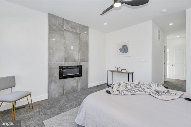 bedroom with carpet, ceiling fan, heating unit, and a tiled fireplace