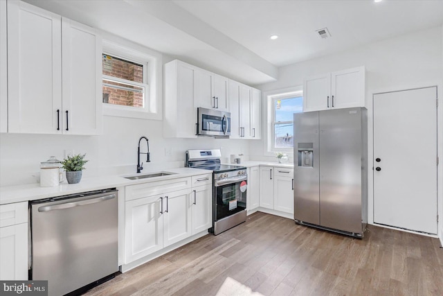 kitchen featuring stainless steel appliances, white cabinetry, light hardwood / wood-style floors, and sink