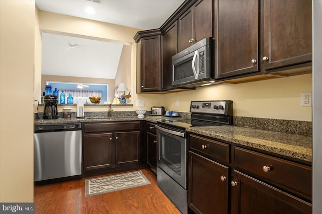 kitchen featuring dark hardwood / wood-style flooring, stainless steel appliances, ceiling fan, sink, and dark stone countertops