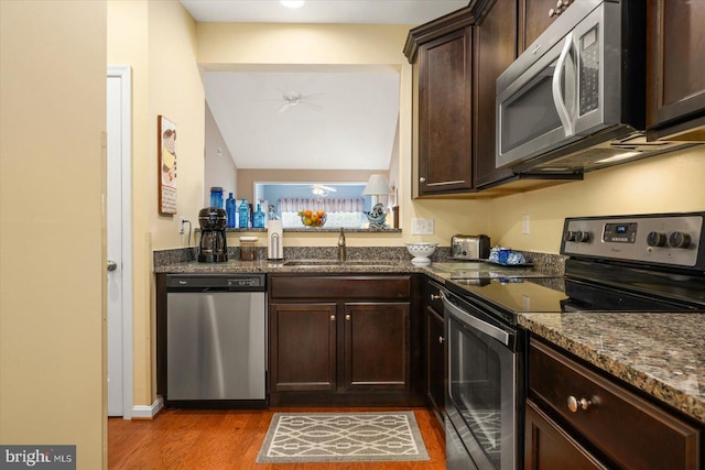 kitchen featuring light wood-type flooring, dark stone counters, stainless steel appliances, ceiling fan, and sink