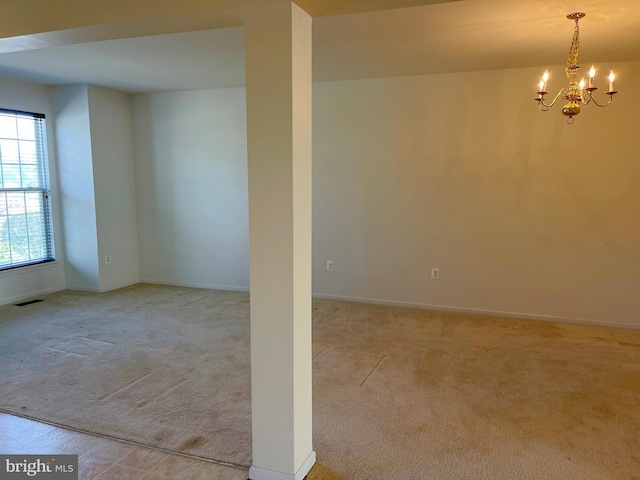 carpeted spare room featuring a chandelier, visible vents, and baseboards