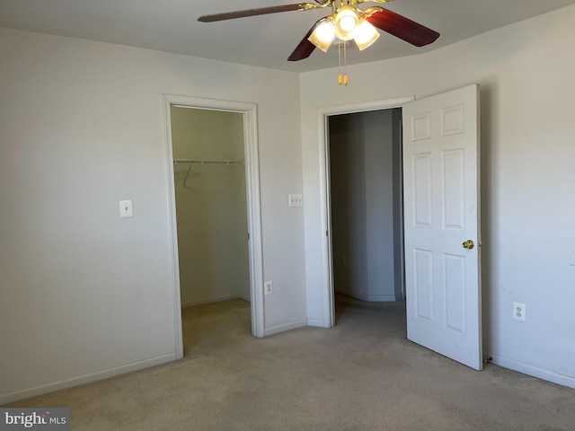 unfurnished bedroom featuring a walk in closet, a closet, light colored carpet, a ceiling fan, and baseboards