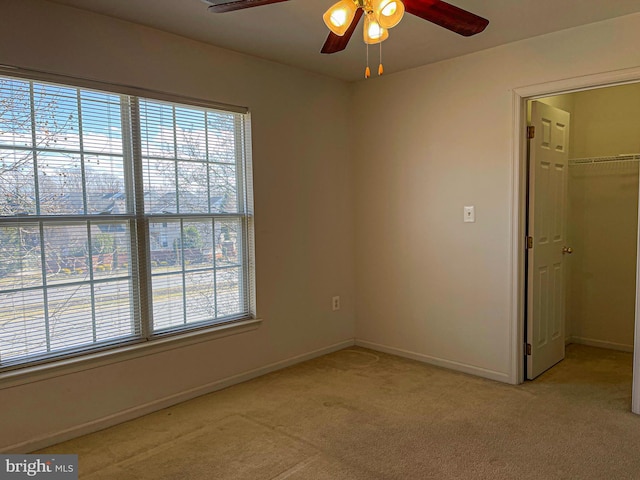 unfurnished bedroom featuring a walk in closet, a closet, light carpet, ceiling fan, and baseboards