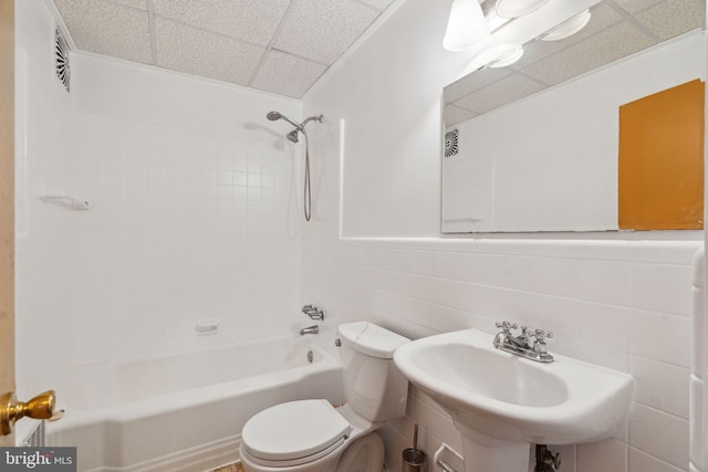 full bathroom featuring tiled shower / bath, sink, tile walls, toilet, and a drop ceiling