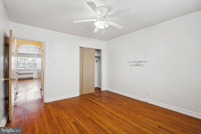 unfurnished bedroom featuring hardwood / wood-style flooring, ceiling fan, radiator heating unit, and a closet