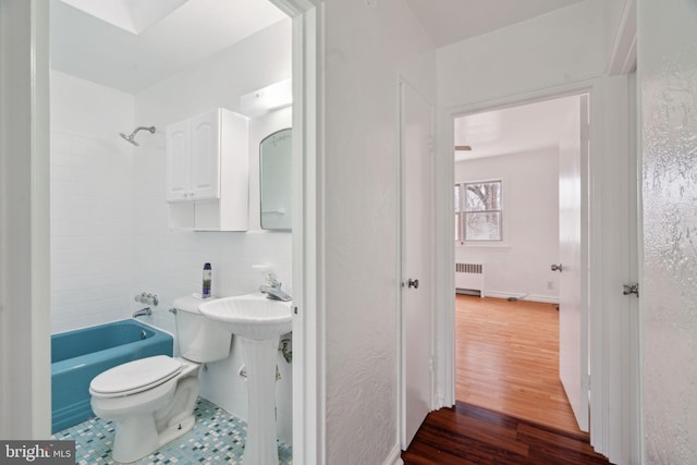 full bathroom featuring radiator heating unit, sink, hardwood / wood-style flooring, tiled shower / bath combo, and toilet