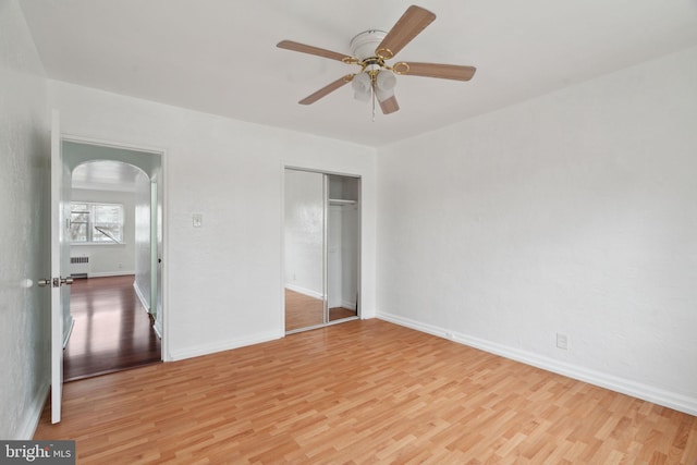 unfurnished bedroom featuring ceiling fan, radiator, light hardwood / wood-style floors, and a closet