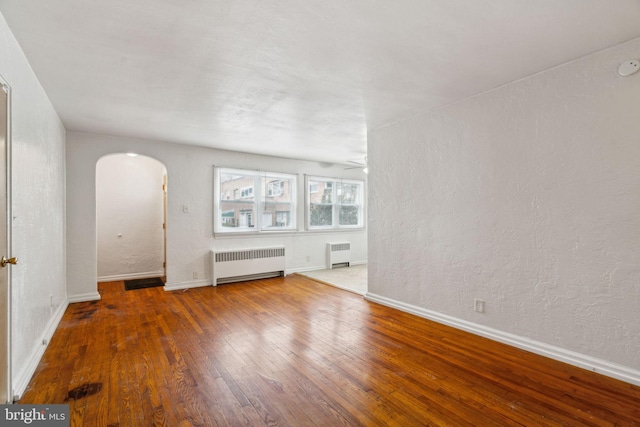 unfurnished living room with dark wood-type flooring, ceiling fan, and radiator heating unit