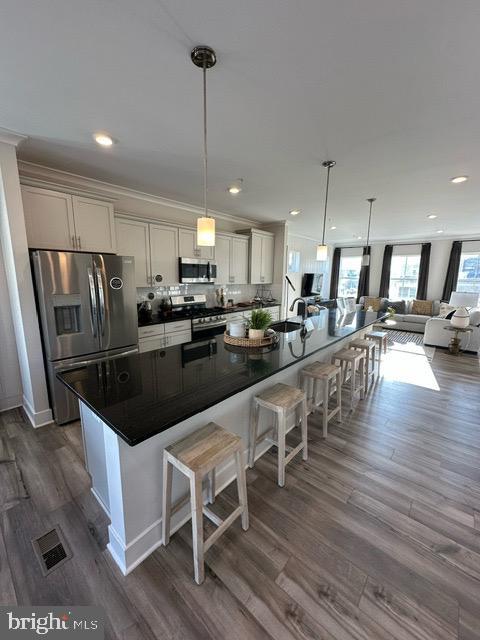 kitchen with dark hardwood / wood-style floors, pendant lighting, a breakfast bar, white cabinets, and appliances with stainless steel finishes