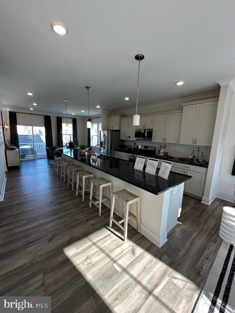 kitchen featuring hanging light fixtures, stainless steel appliances, dark hardwood / wood-style flooring, a spacious island, and a breakfast bar area