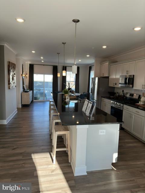 kitchen with white cabinetry, a center island, hanging light fixtures, stainless steel appliances, and a kitchen bar