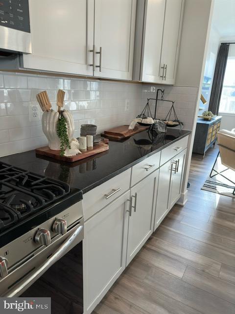 kitchen with tasteful backsplash, stainless steel range with gas cooktop, white cabinetry, and light wood-type flooring