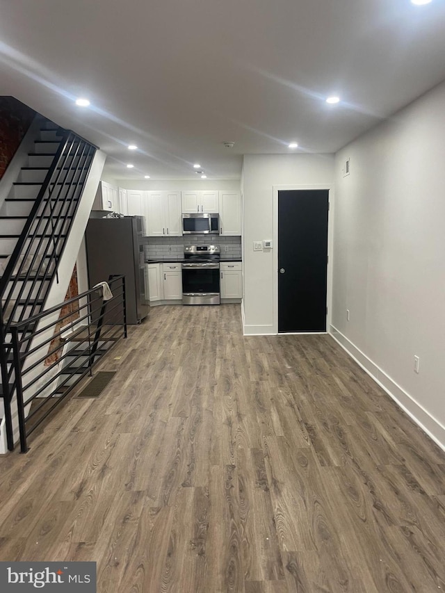 kitchen featuring wood finished floors, baseboards, stainless steel appliances, decorative backsplash, and white cabinets