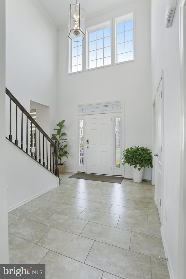 entrance foyer with light tile patterned floors, a chandelier, a high ceiling, and ornamental molding