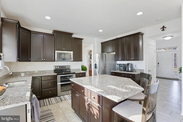 kitchen with light stone countertops, appliances with stainless steel finishes, a kitchen island, and sink