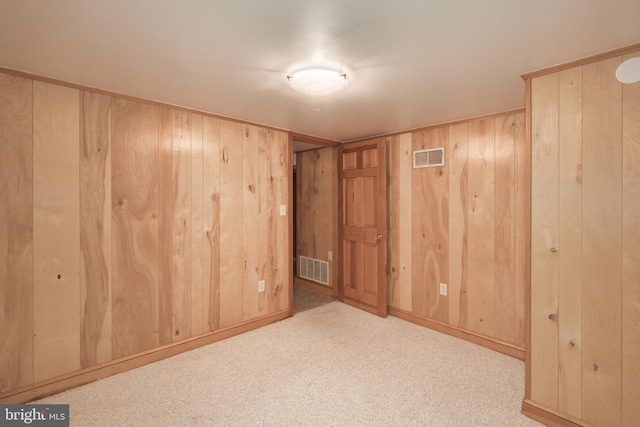 carpeted empty room featuring wood walls