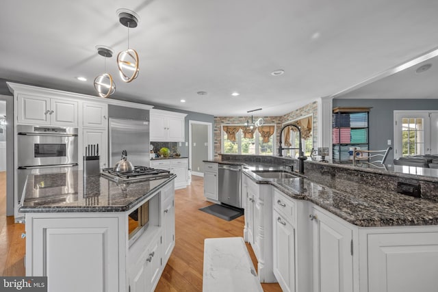 kitchen featuring a large island with sink, white cabinetry, built in appliances, and pendant lighting