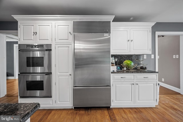 kitchen featuring white cabinets, appliances with stainless steel finishes, decorative backsplash, and dark stone countertops