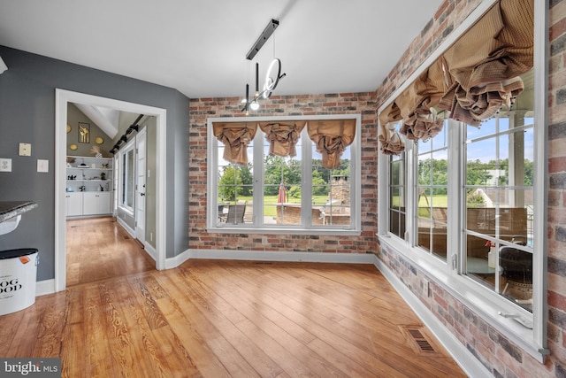 unfurnished dining area featuring hardwood / wood-style floors and brick wall