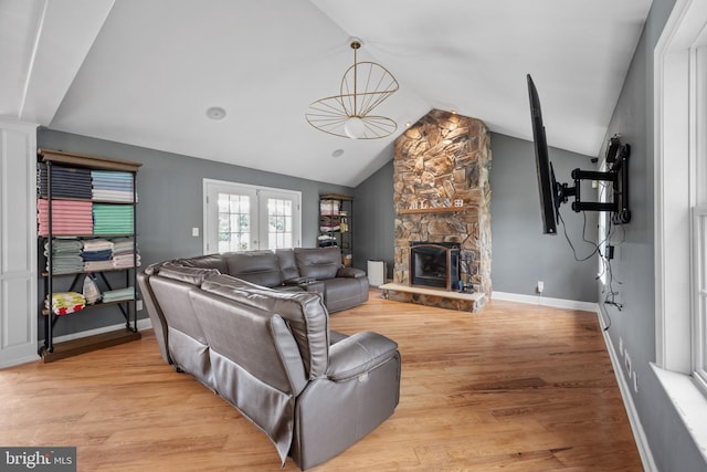 living room featuring light hardwood / wood-style floors, lofted ceiling, a fireplace, and french doors