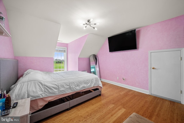 bedroom with an inviting chandelier, vaulted ceiling, and hardwood / wood-style flooring