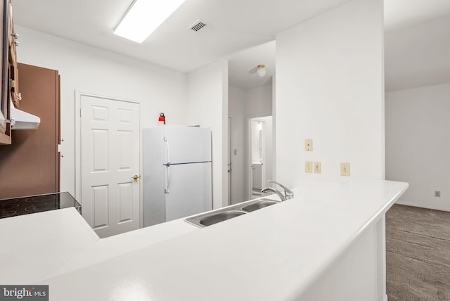 kitchen with carpet flooring, white fridge, sink, and kitchen peninsula