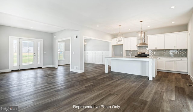 kitchen featuring an island with sink, pendant lighting, decorative backsplash, a breakfast bar, and white cabinets