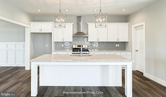 kitchen featuring white cabinets, light stone countertops, wall chimney exhaust hood, and an island with sink