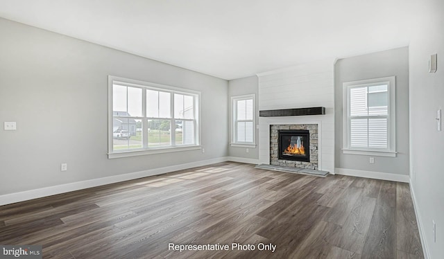 unfurnished living room with dark hardwood / wood-style floors, a stone fireplace, and a healthy amount of sunlight