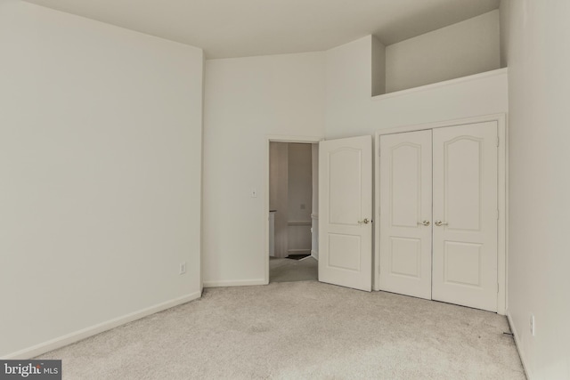 unfurnished bedroom with a closet, light carpet, and a towering ceiling