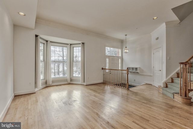 empty room with a wall mounted AC, ornamental molding, a notable chandelier, and light wood-type flooring