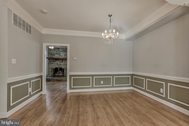 unfurnished dining area featuring an inviting chandelier, crown molding, a fireplace, and wood-type flooring