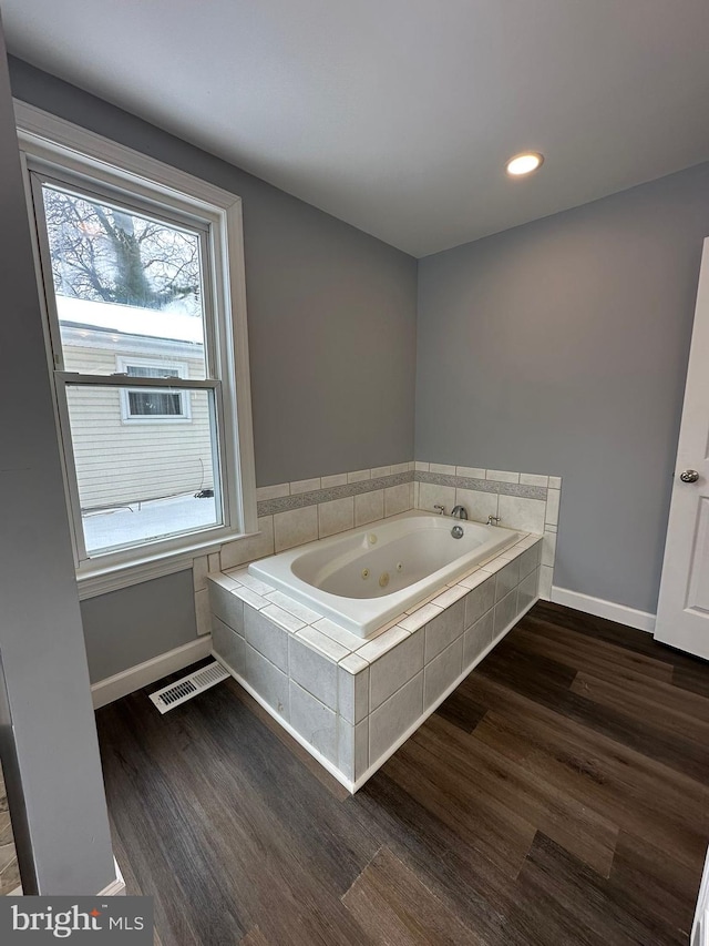 bathroom featuring wood-type flooring and a relaxing tiled tub