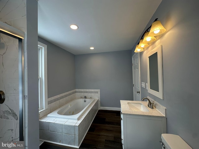 bathroom with hardwood / wood-style floors, vanity, a relaxing tiled tub, and toilet