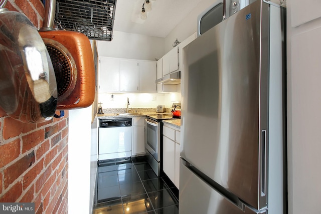 kitchen featuring white cabinets, sink, light stone counters, stainless steel appliances, and brick wall